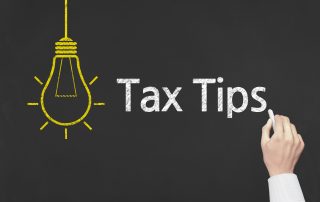A hand writing "Tax Tips" on a black chalkboard next to a drawing of a yellow light bulb.
