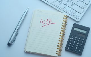 A pen, a notepad, a calculator, and the corner of a keyboard sit on a white background. "401K" is written and underlined in large red print on the notepad.